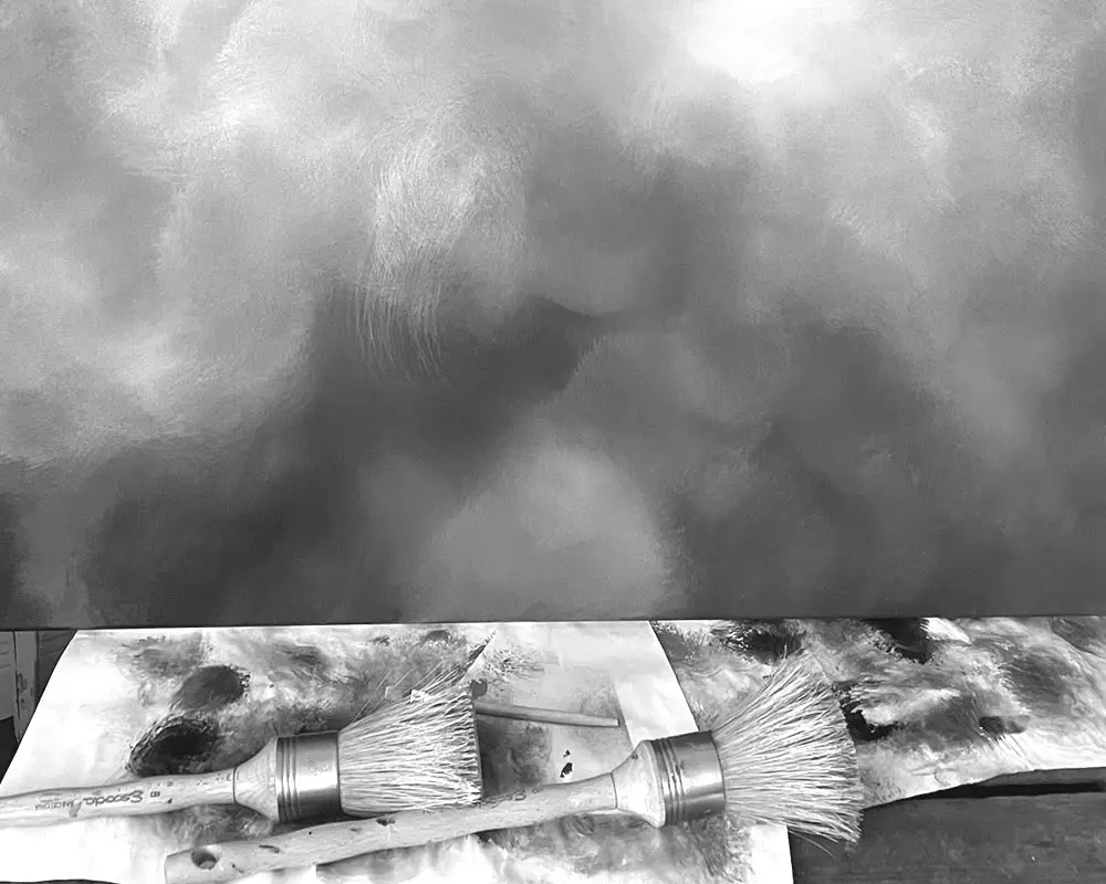 Nahaufnahme von zwei runden Pinseln vor einem abstrakten Wolkenbild von Christin von Wels. Die Schwarz-Weiß-Fotografie zeigt die feinen Strukturen einer atmosphärischen Himmelslandschaft und den künstlerischen Prozess im Atelier.
